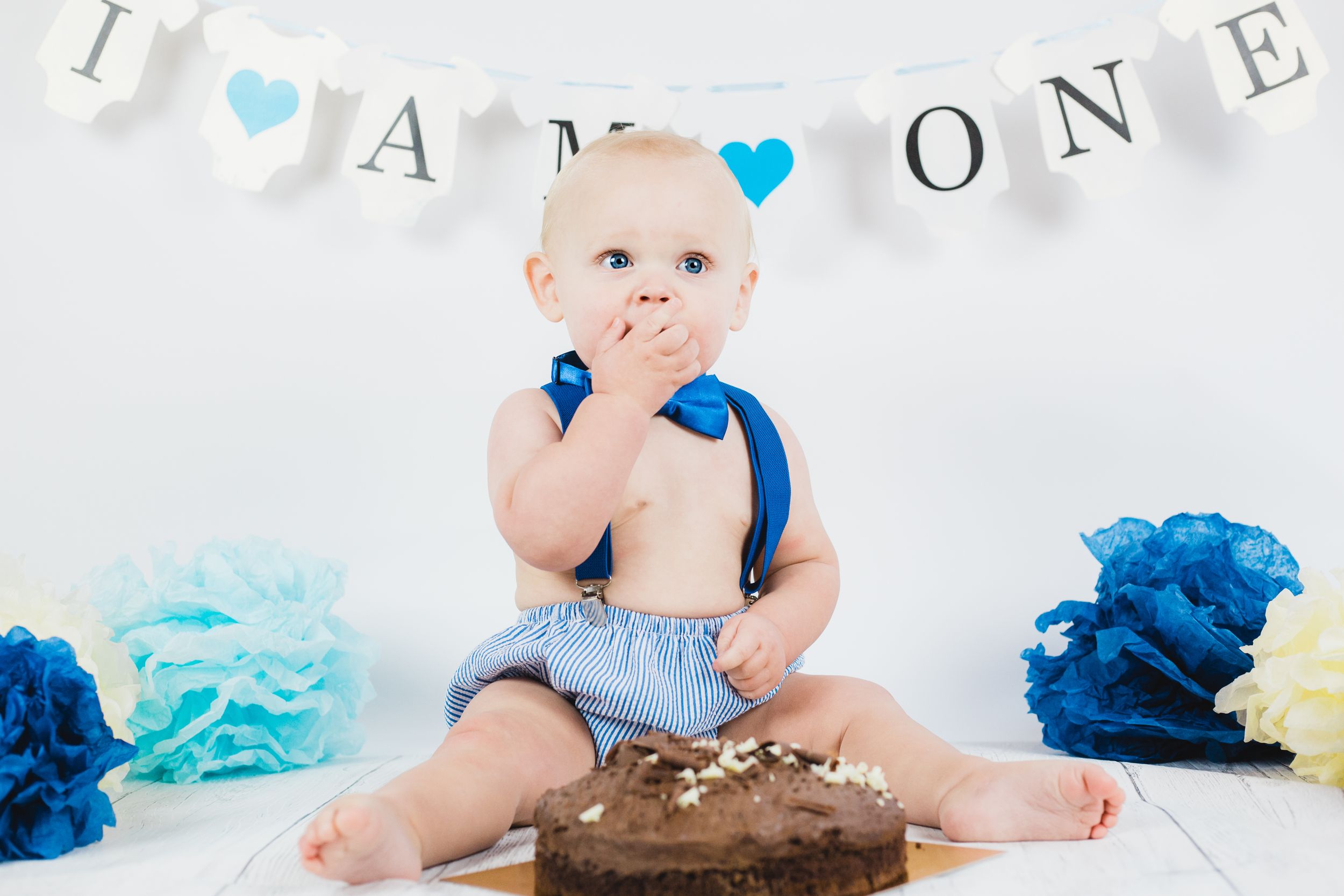 Birthday party scene with blue pom poms and 'ONE' banner in white and gold.