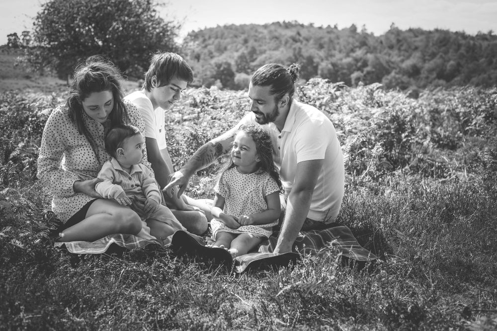 Family lying together on grassy hill during black and white outdoor photoshoot.
