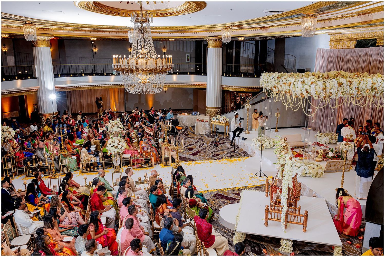 Grand ballroom wedding reception with circular seating arrangement and suspended floral decorations.