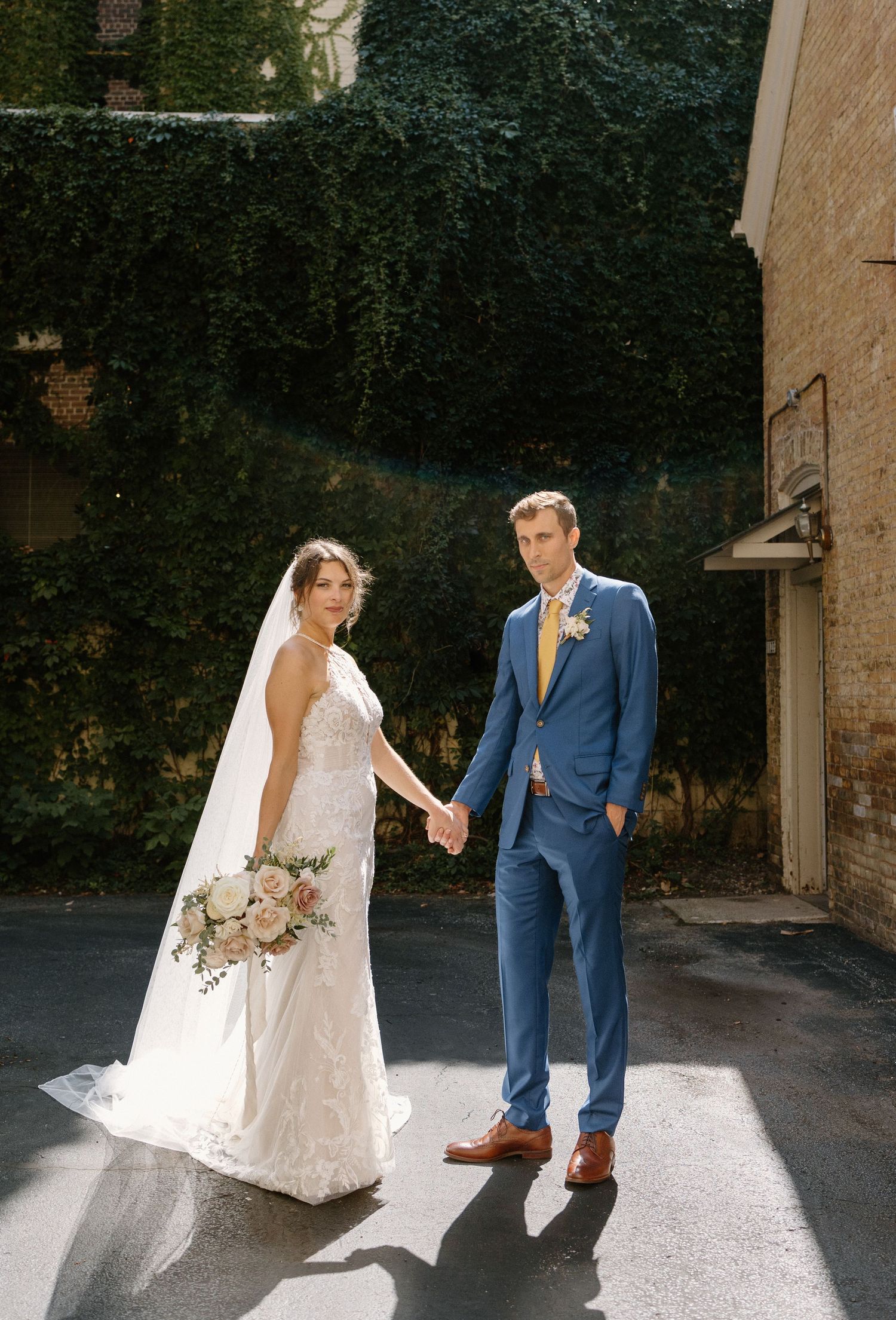 Elegant wedding couple in navy suit and white gown pose together in a romantic outdoor setting.
