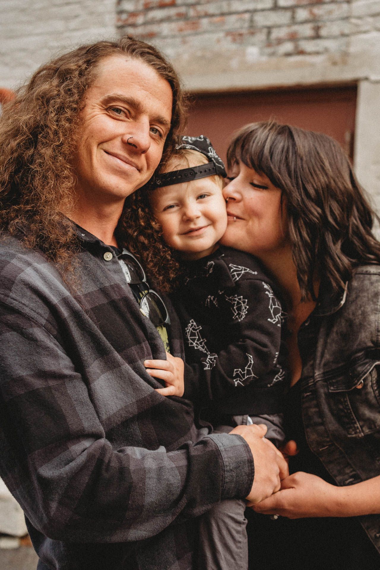Loving family moment captured against rustic brick wall background in warm lighting.