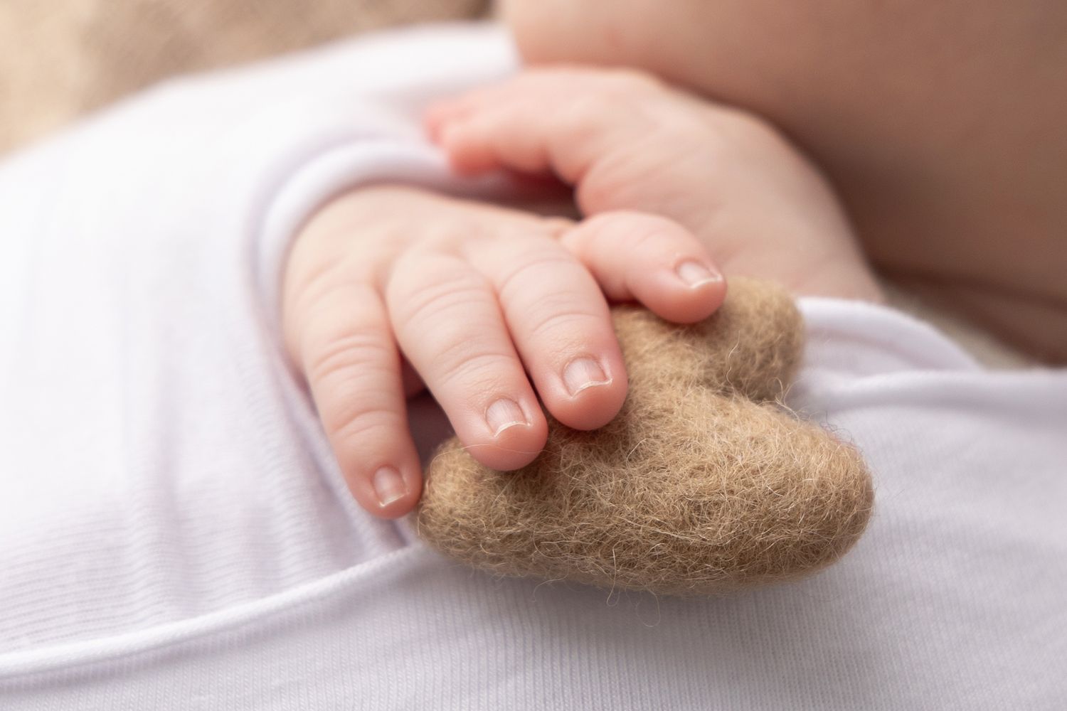 Close-up of baby's tiny hand grasping a soft brown teddy bear.