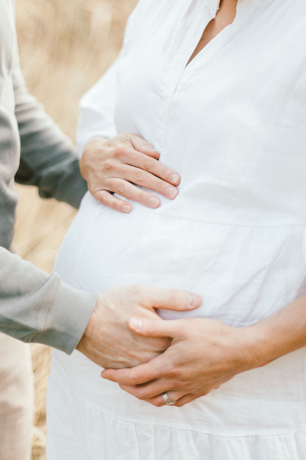 Close-up of hands tenderly cradling a pregnant belly in white dress.