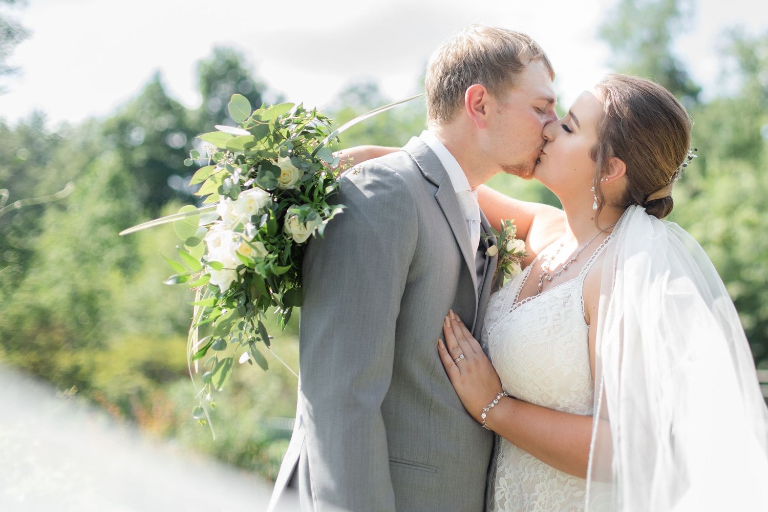 Romantic wedding couple shares intimate moments in a sun-dappled outdoor setting with flowing white veil.