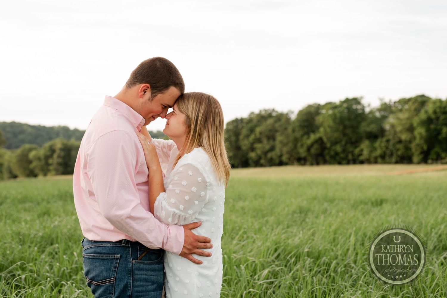 A romantic couple shares an intimate moment in a grassy field at sunset.