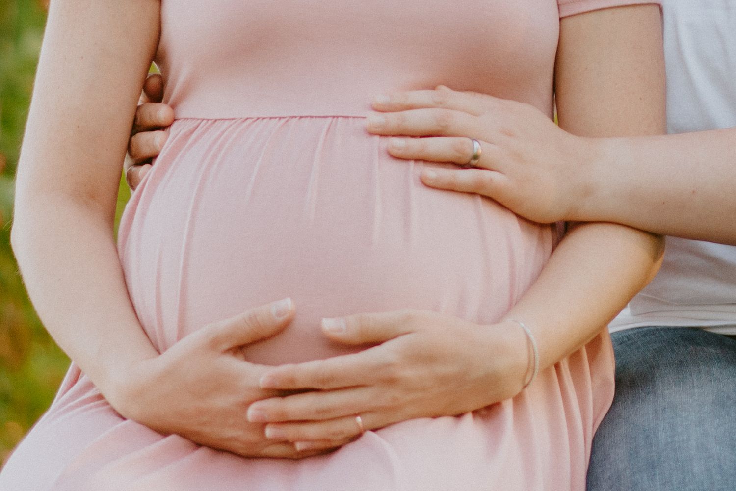 Pregnancy in pink dress with partners hands on tummy