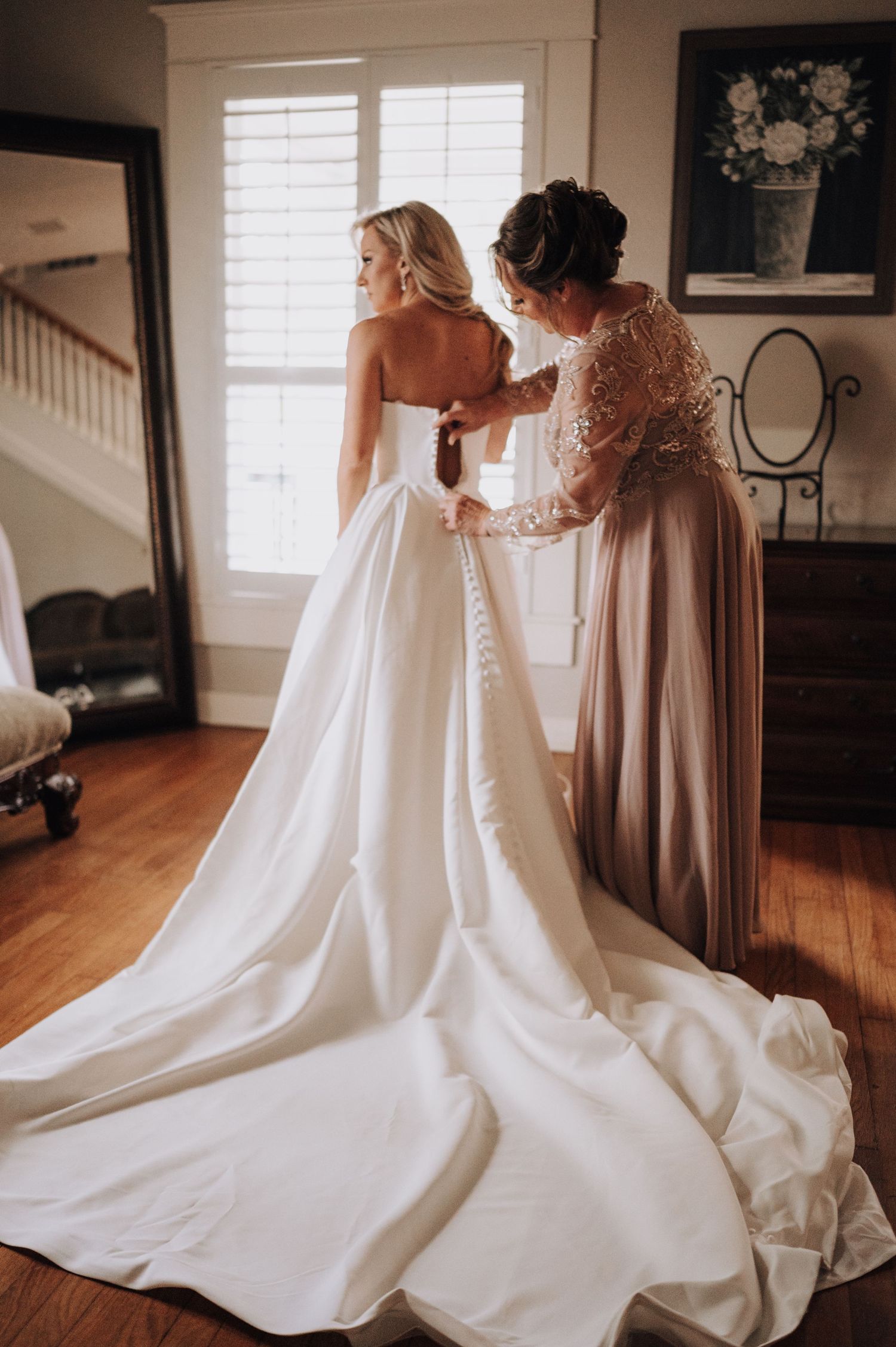 Elegant white wedding dress being buttoned up in sunlit room.
