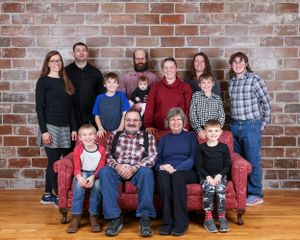 Large multigenerational family portrait posed in front of a red brick wall indoors.