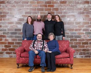 Family of six posing on a red couch in front of a brick wall for a portrait.