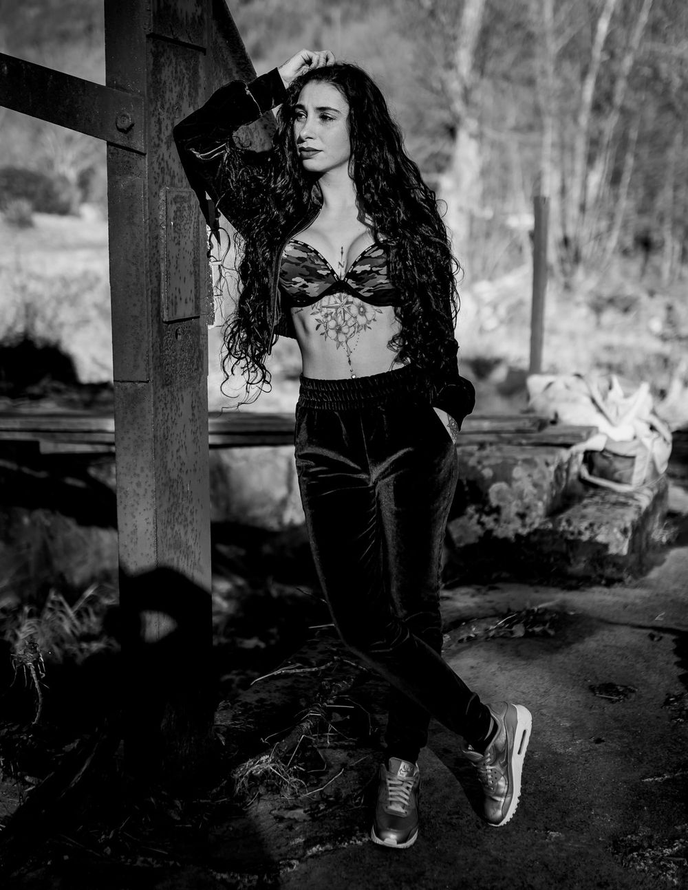Dramatic black and white portrait showing a pose against wooden beams in an outdoor setting.