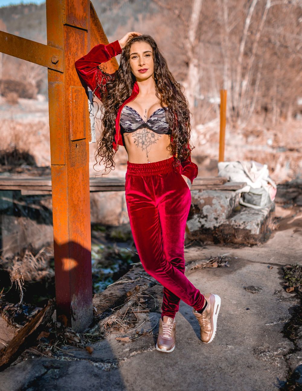 Fashion portrait featuring red velvet outfit against rustic wooden architecture and winter landscape.