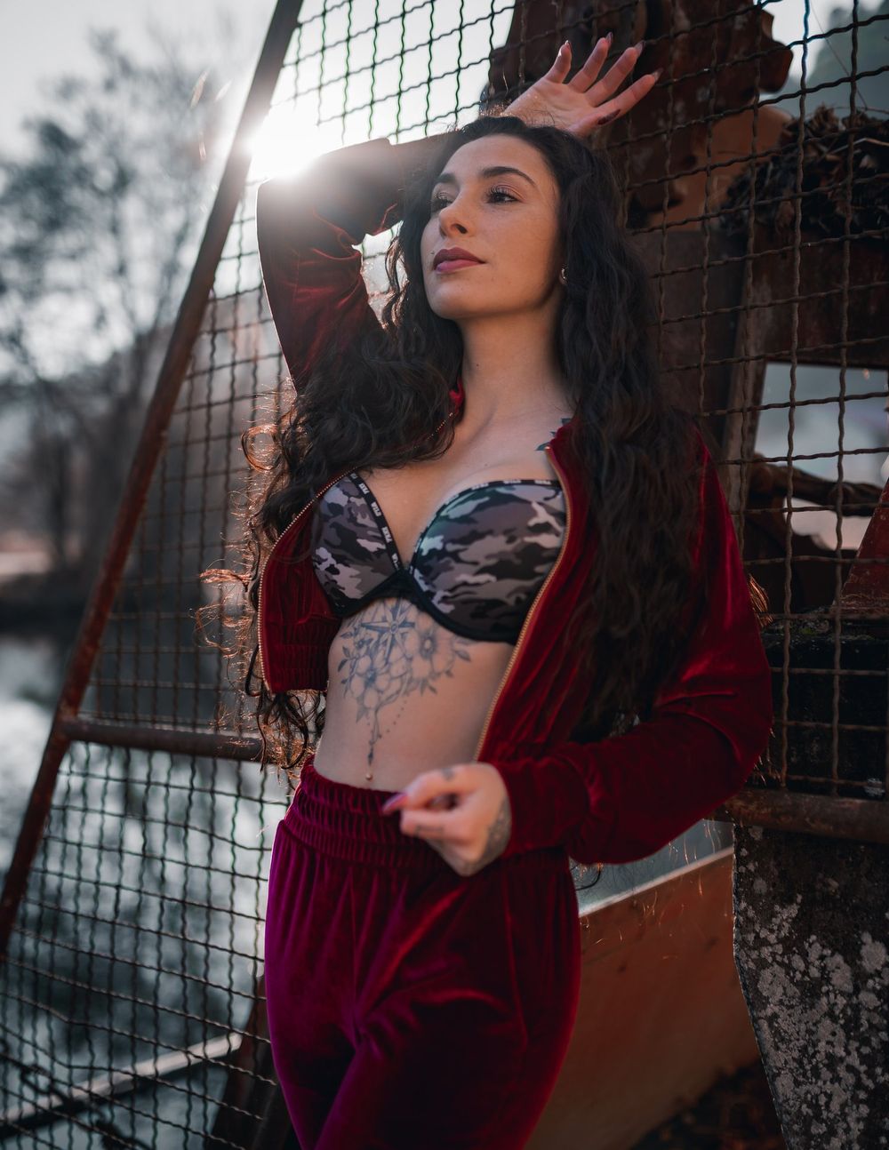 Fashion portrait featuring red velvet and lace against industrial metalwork and sunlight.