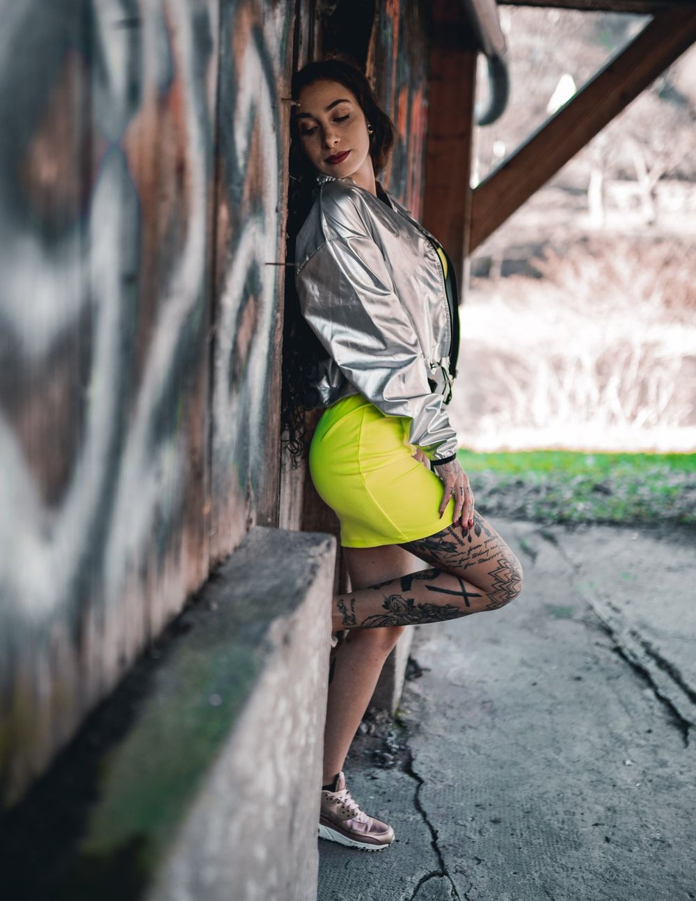 Street fashion portrait with silver jacket and neon yellow skirt against industrial background.