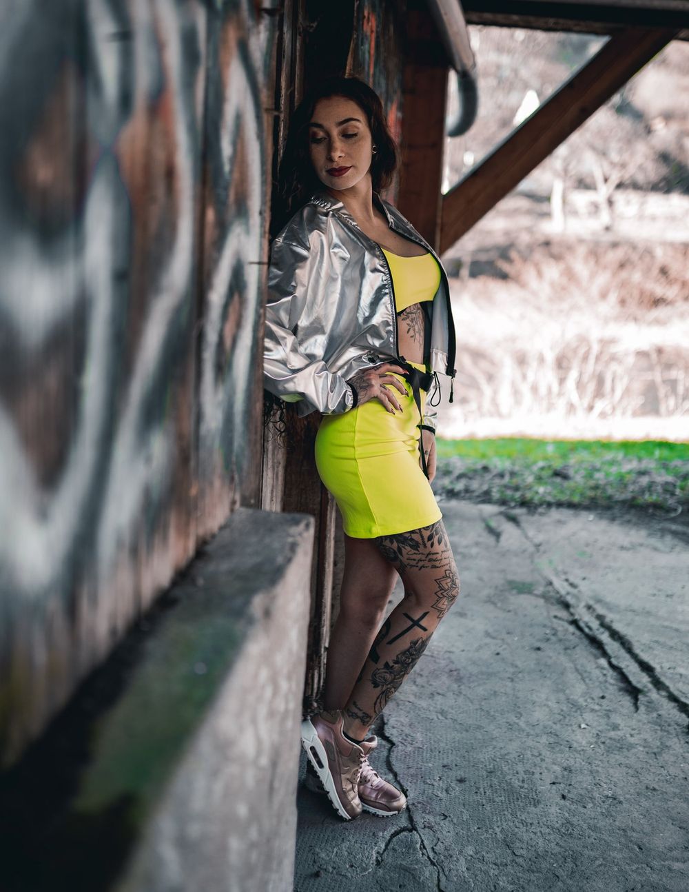 Fashion portrait featuring silver jacket and neon yellow skirt in industrial setting.