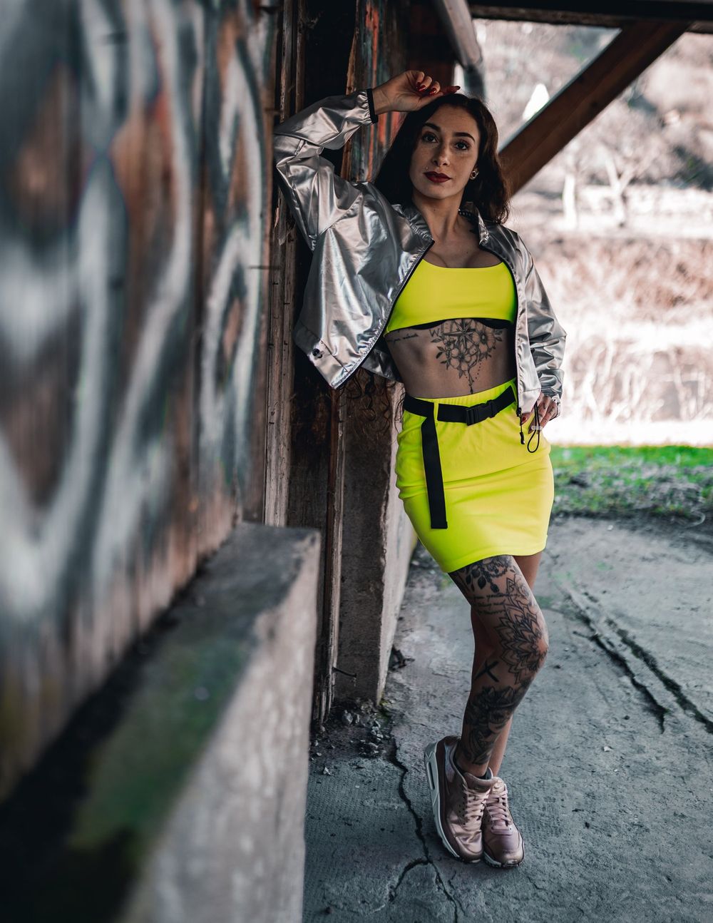 Urban fashion shot featuring metallic jacket and yellow two-piece set against concrete backdrop.