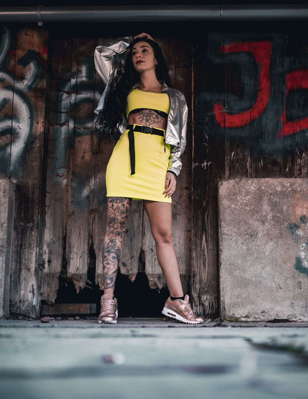 Urban fashion portrait featuring metallic and neon yellow outfit against textured wall.