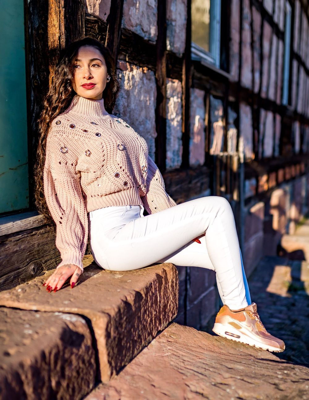 Stylish winter outfit with beige sweater and white pants photographed against historic timber architecture.