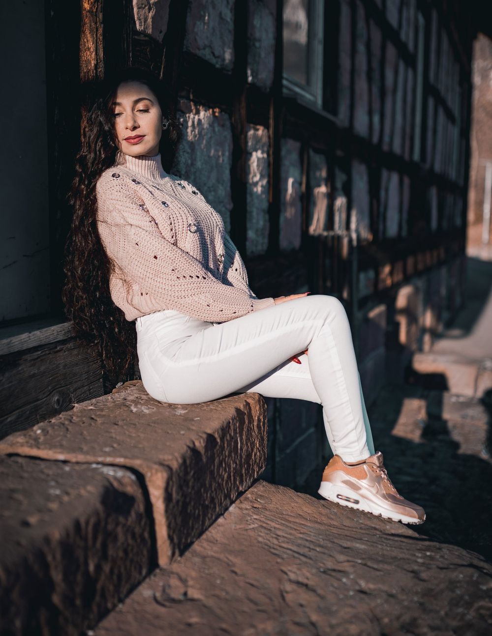 Fashion photography showcasing a cable knit sweater and white jeans in front of a vintage wooden building.