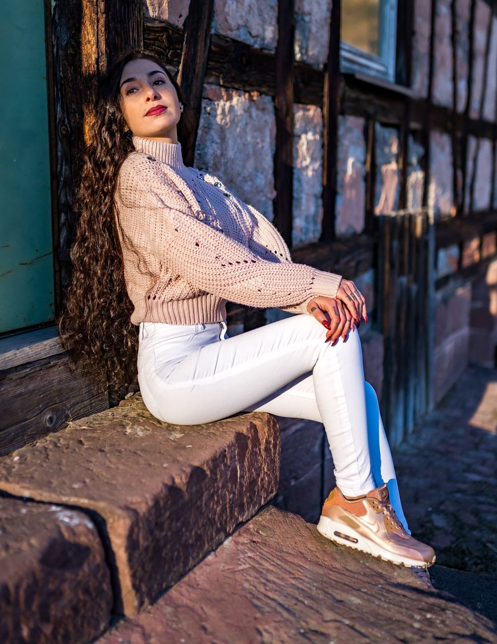 Casual winter fashion look with pink sweater and metallic sneakers against rustic architectural details.