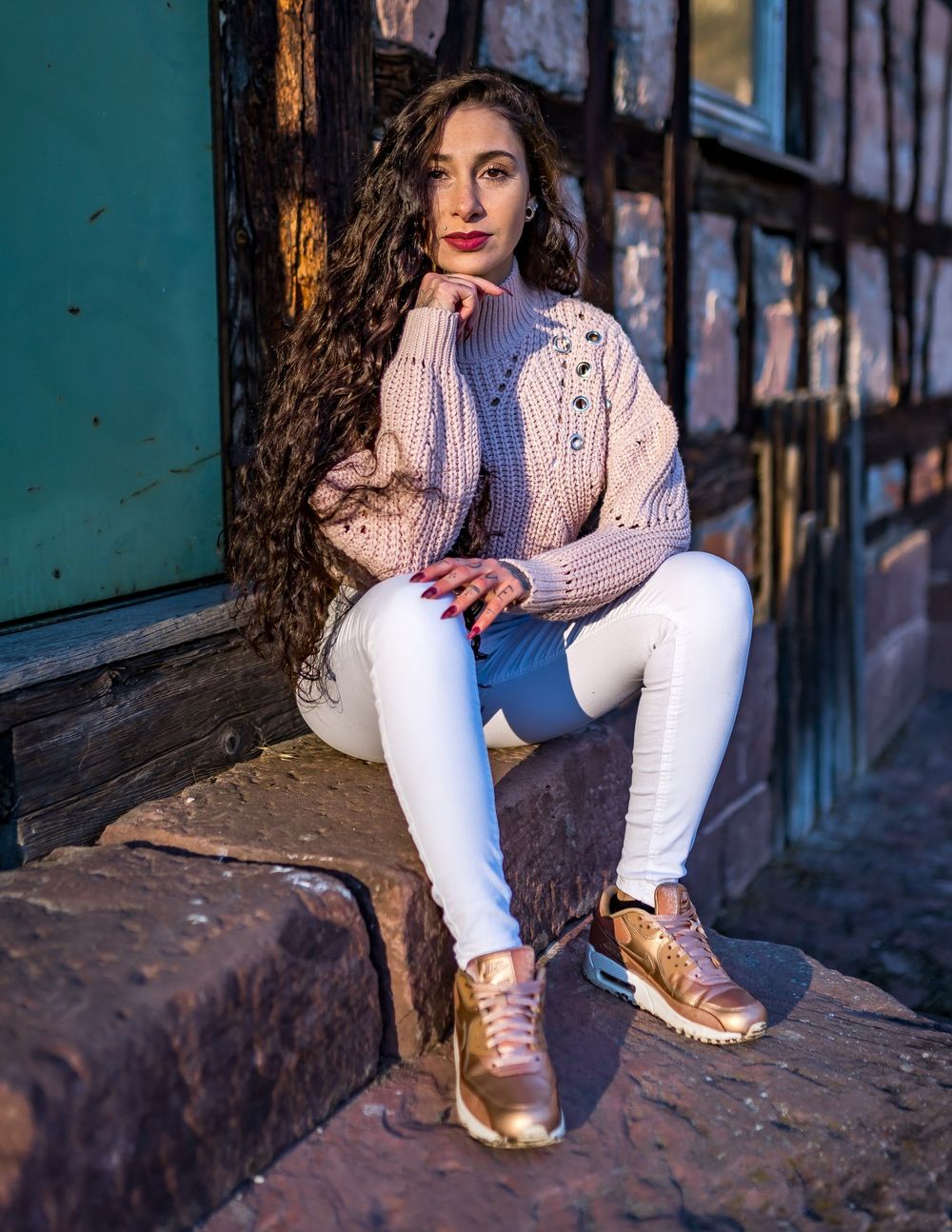 Long wavy hair styled with pale pink sweater and white pants for a fashion photoshoot.