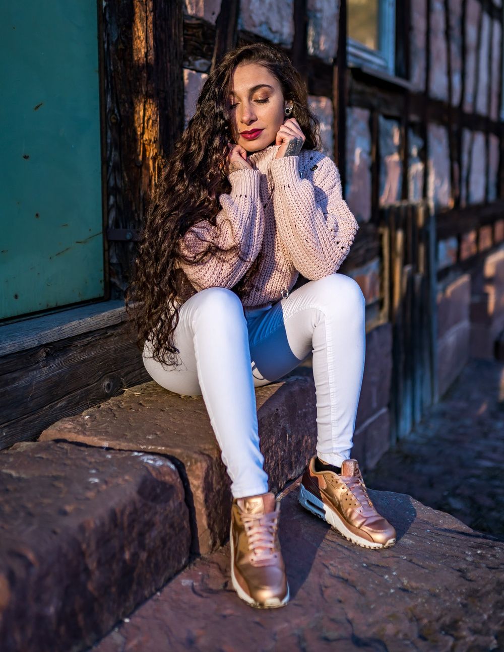 Cozy winter fashion featuring a chunky knit sweater and gold metallic sneakers against industrial backdrop.