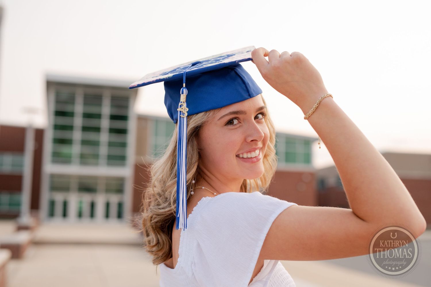 Graduate adjusts blue graduation cap while smiling outdoors.