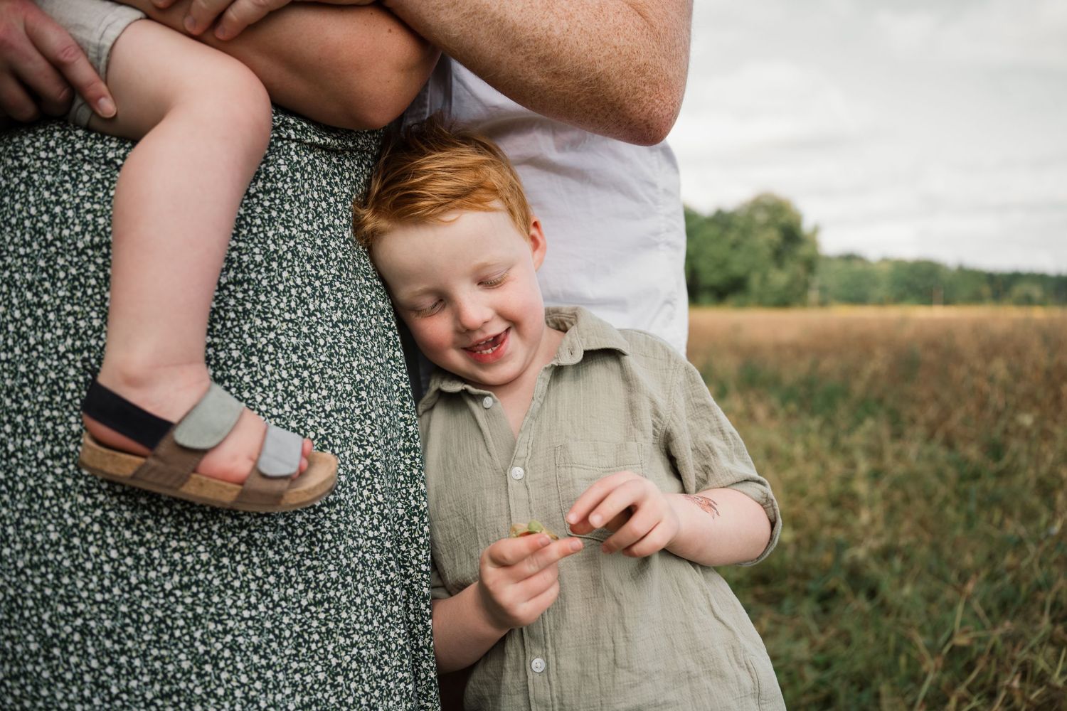 Candid outdoor family moment captured against a rural field backdrop.