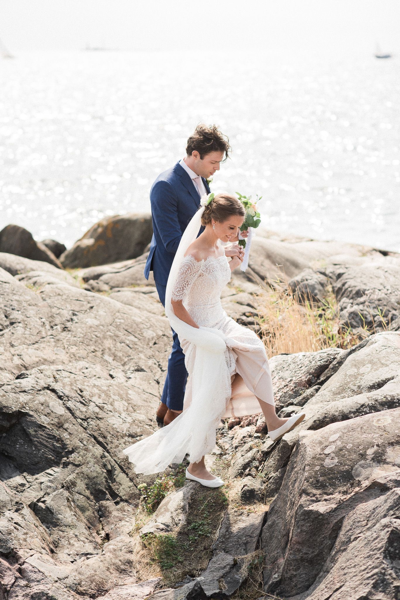 A couple climbing on coastal rocks during their wedding photoshoot.