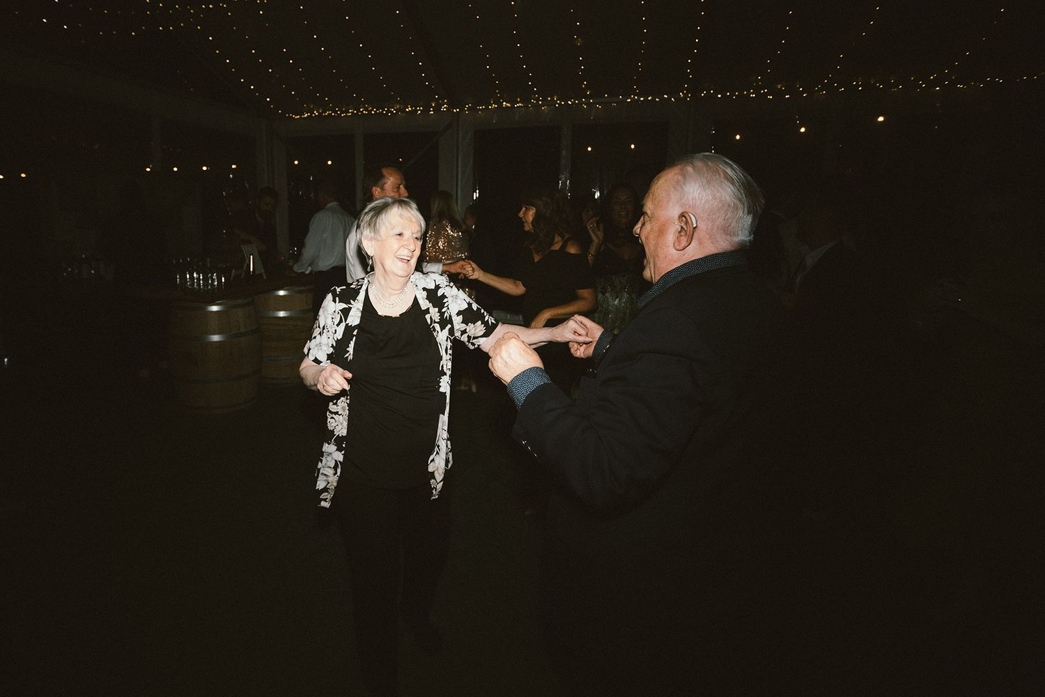 Wedding guests dancing and celebrating under decorative string lights at a reception.