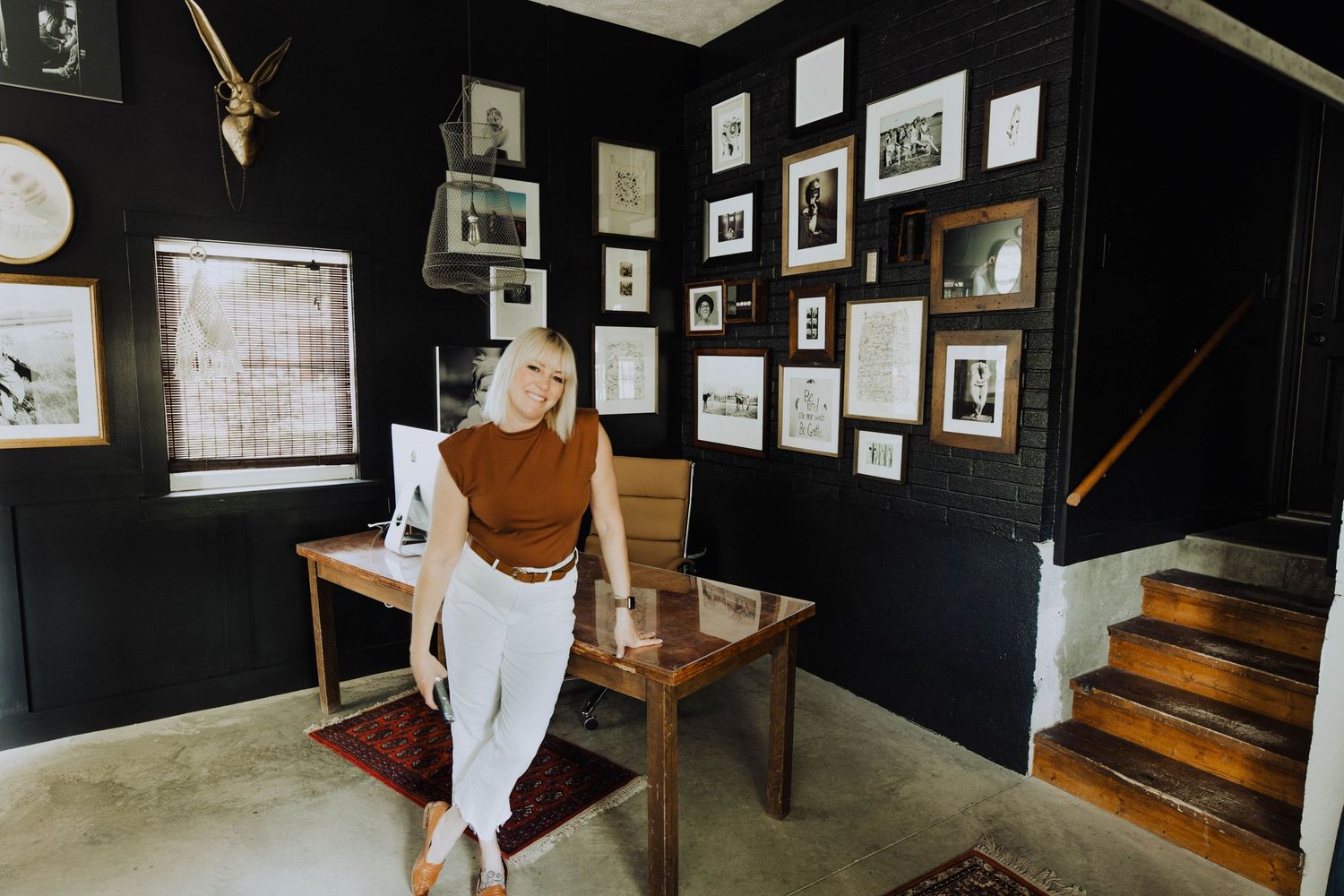 Modern home office with black walls featuring gallery wall and wooden desk.