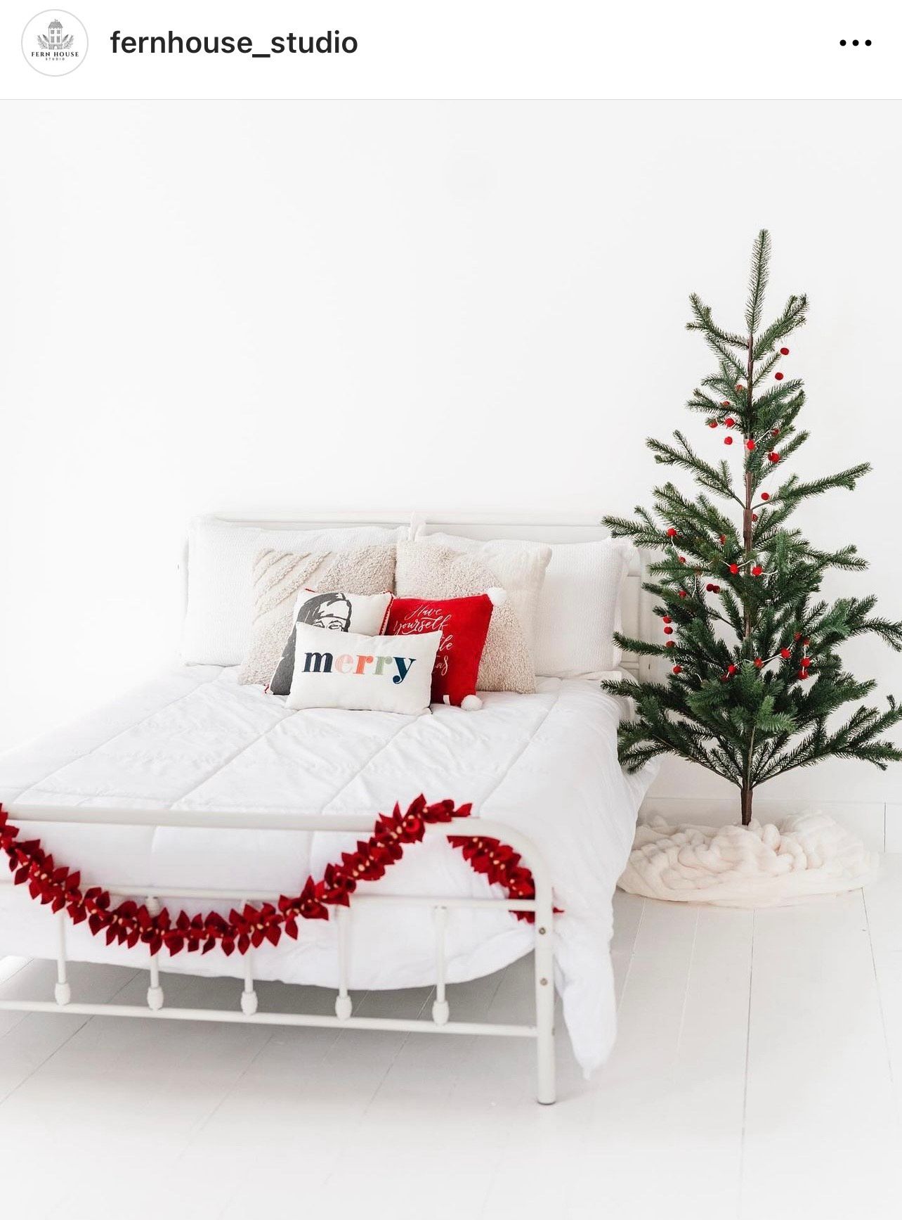 Modern white bedroom with Christmas decorations including a small tree and red garland.
