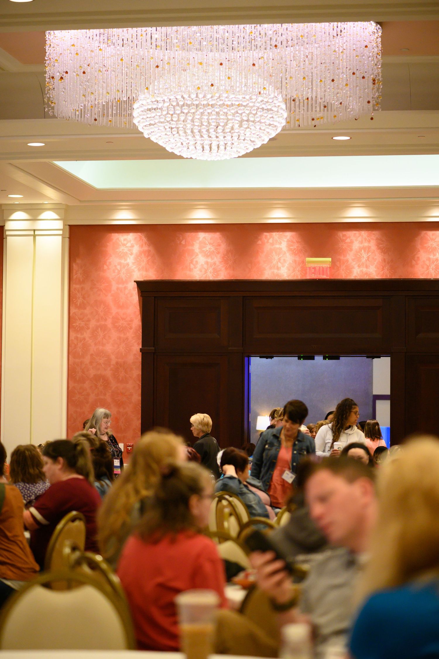 Elegant crystal chandelier hanging above crowd in ballroom setting.