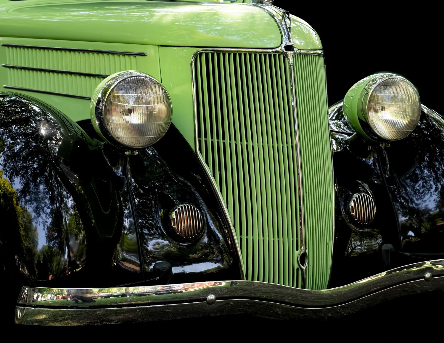 Front grille and headlight detail of a classic green vintage automobile.