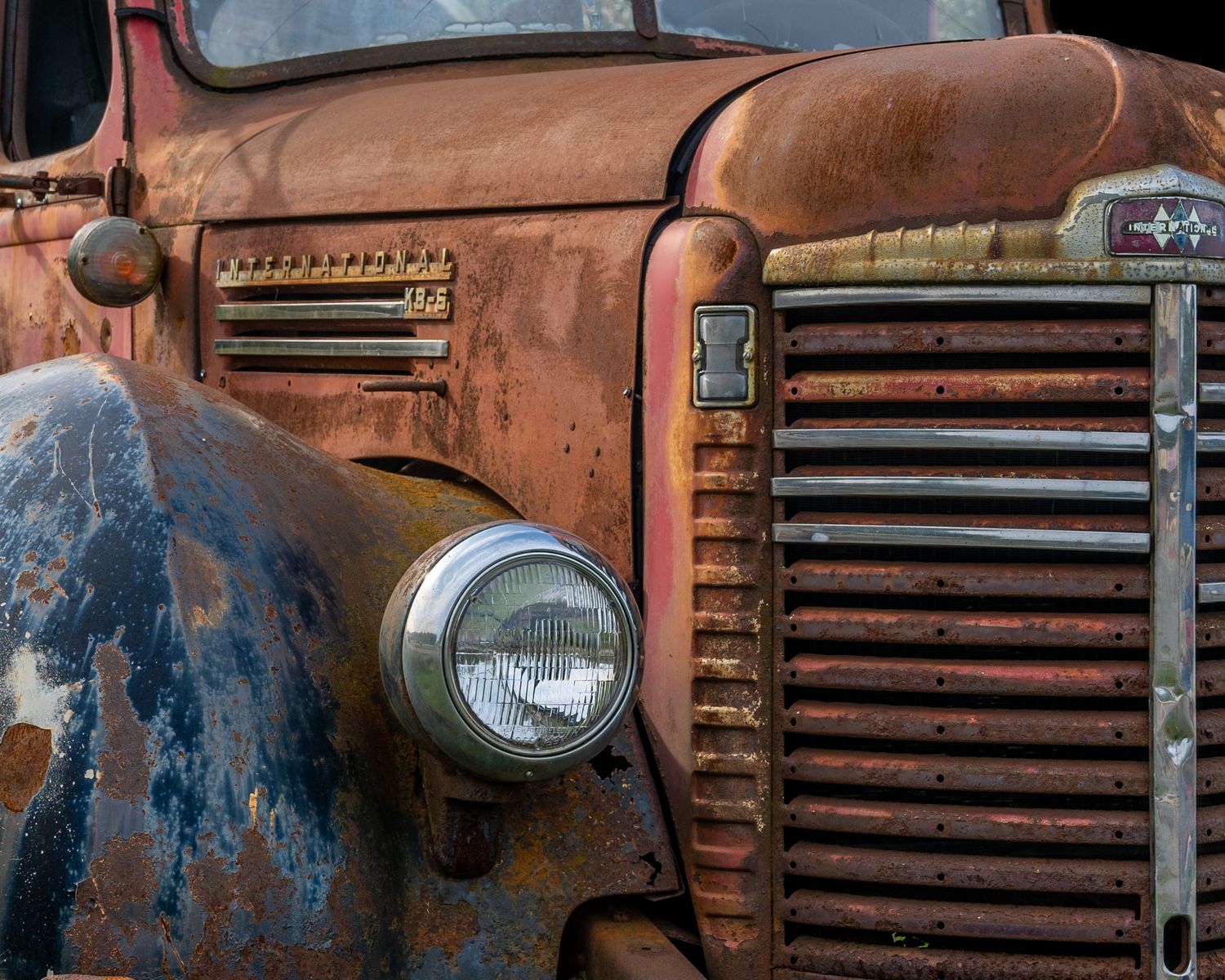 Weathered rusty grille and headlight of an antique farm truck showing patina.