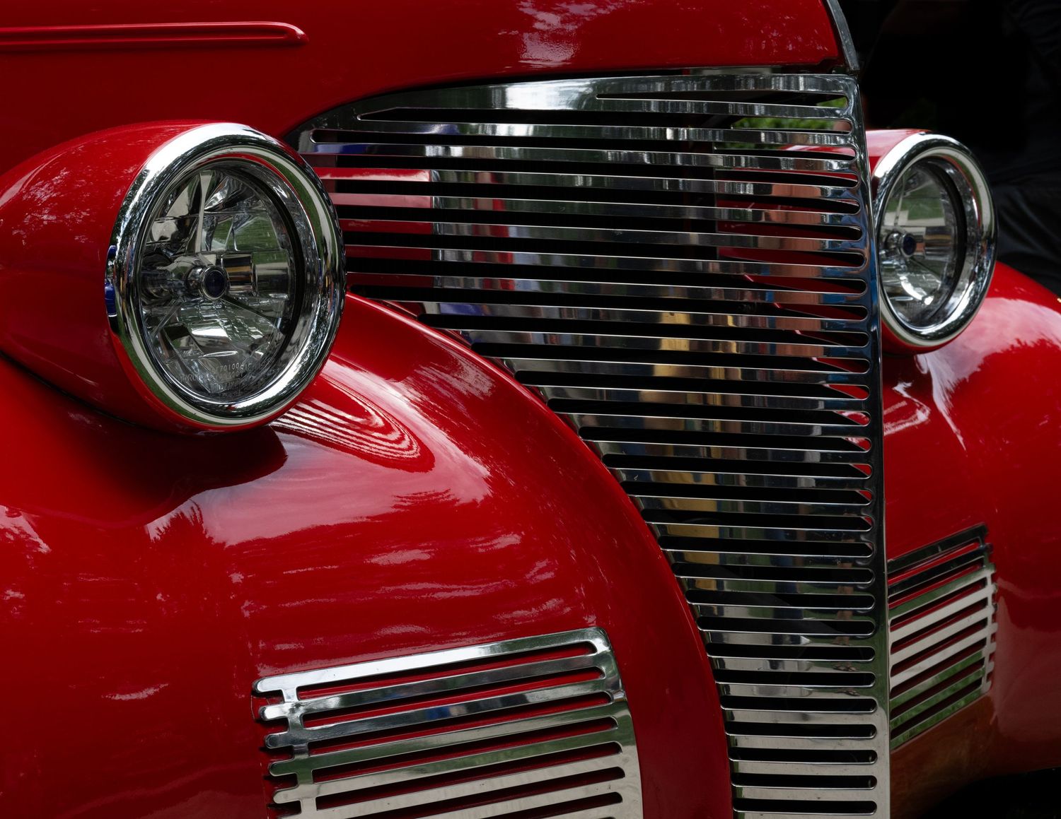 Shiny red classic car front end showing chrome grille and headlight details.