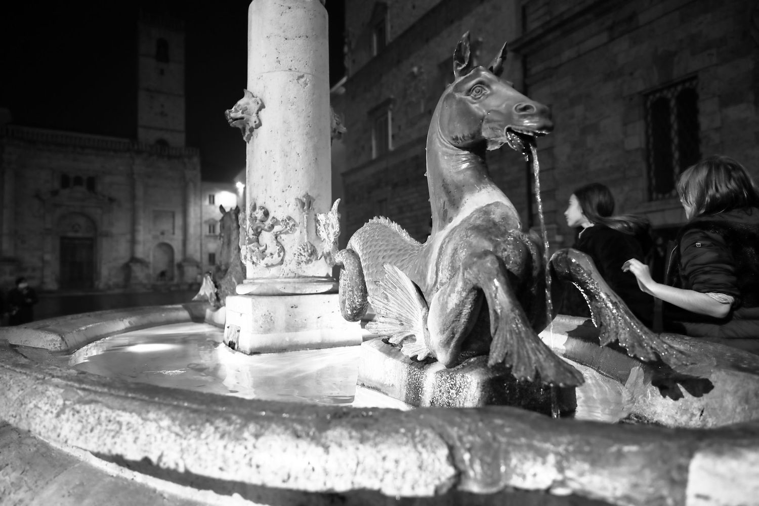 Black and white nighttime image of an ornate horse fountain sculpture in an Italian plaza.