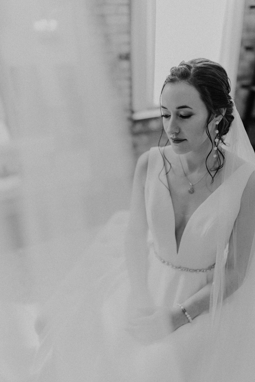 Black and white portrait of bride in V-neck wedding gown with veil softly framing her face.