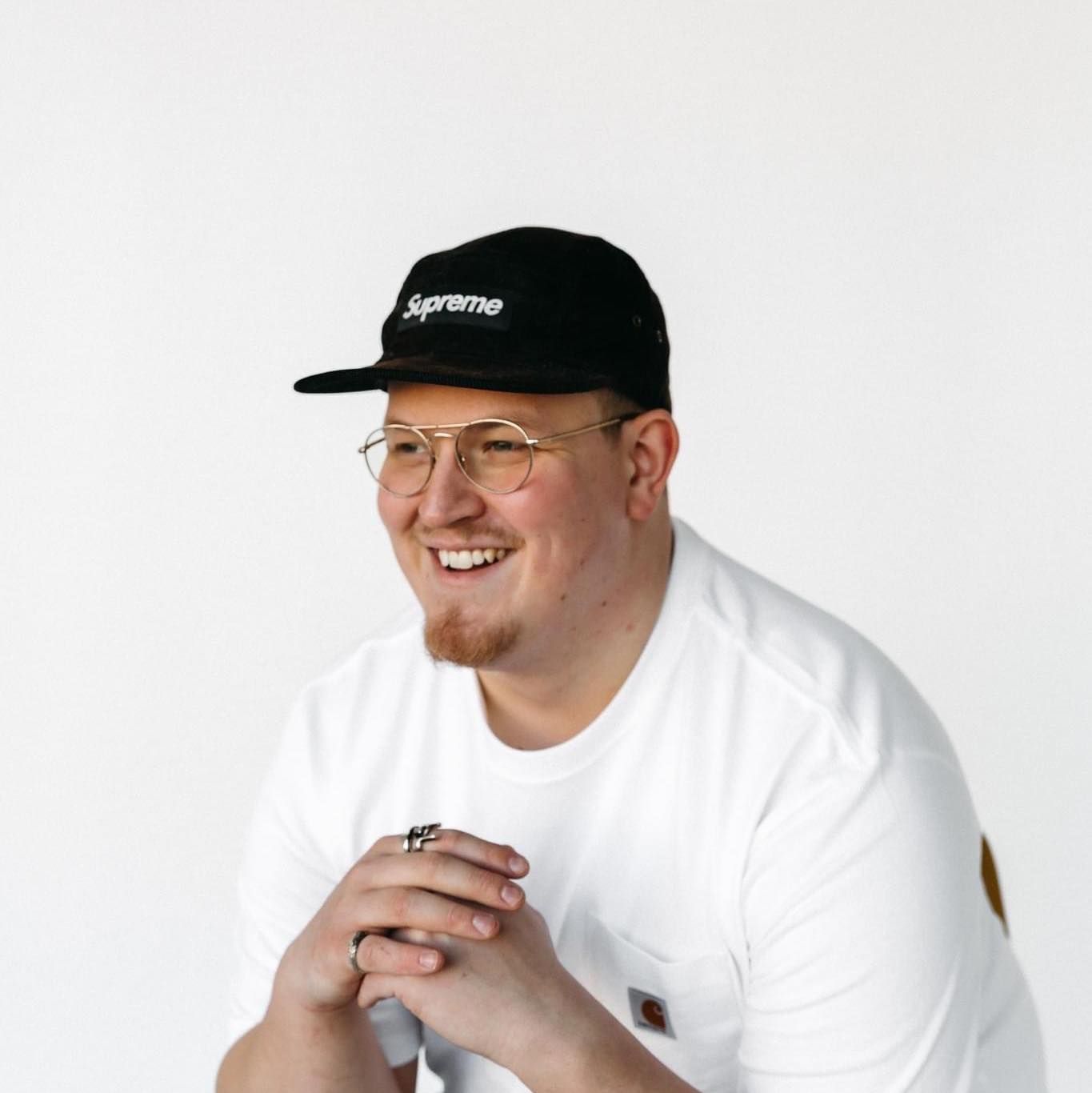 Portrait of photographer wearing black Supreme cap and white t-shirt against white background.