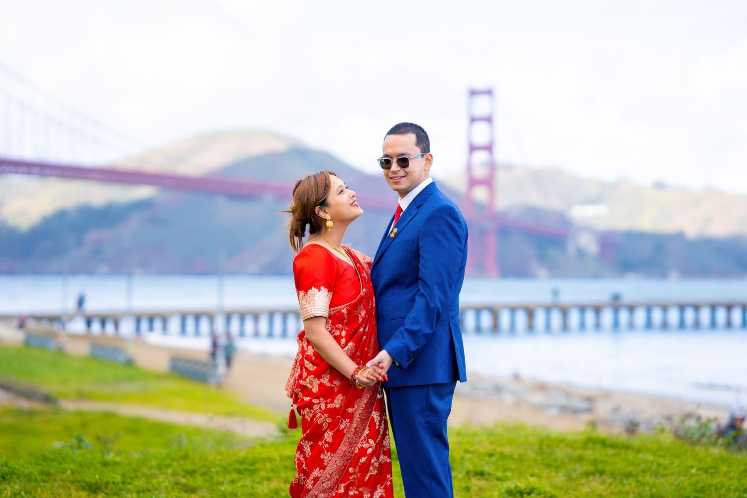 A couple shares a tender moment on a grassy hill overlooking the San Francisco Bay and Golden Gate Bridge.