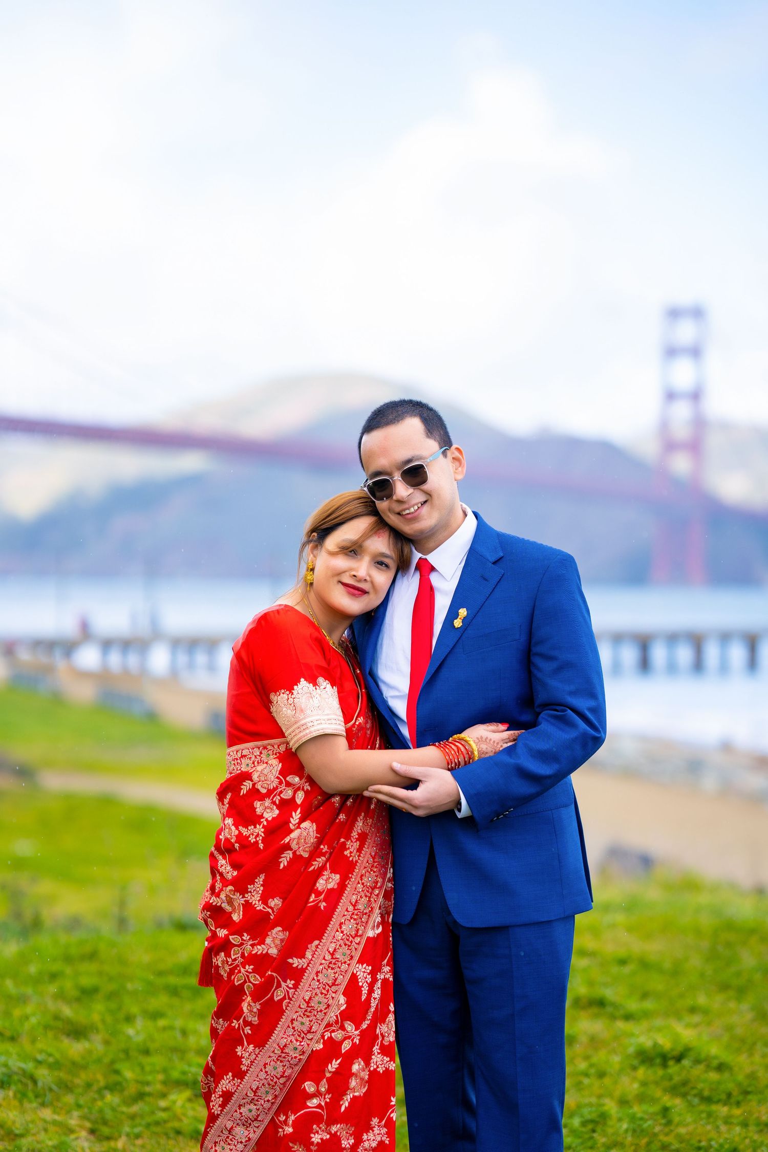 A couple embraces in traditional fusion wedding attire against the iconic Golden Gate Bridge backdrop.