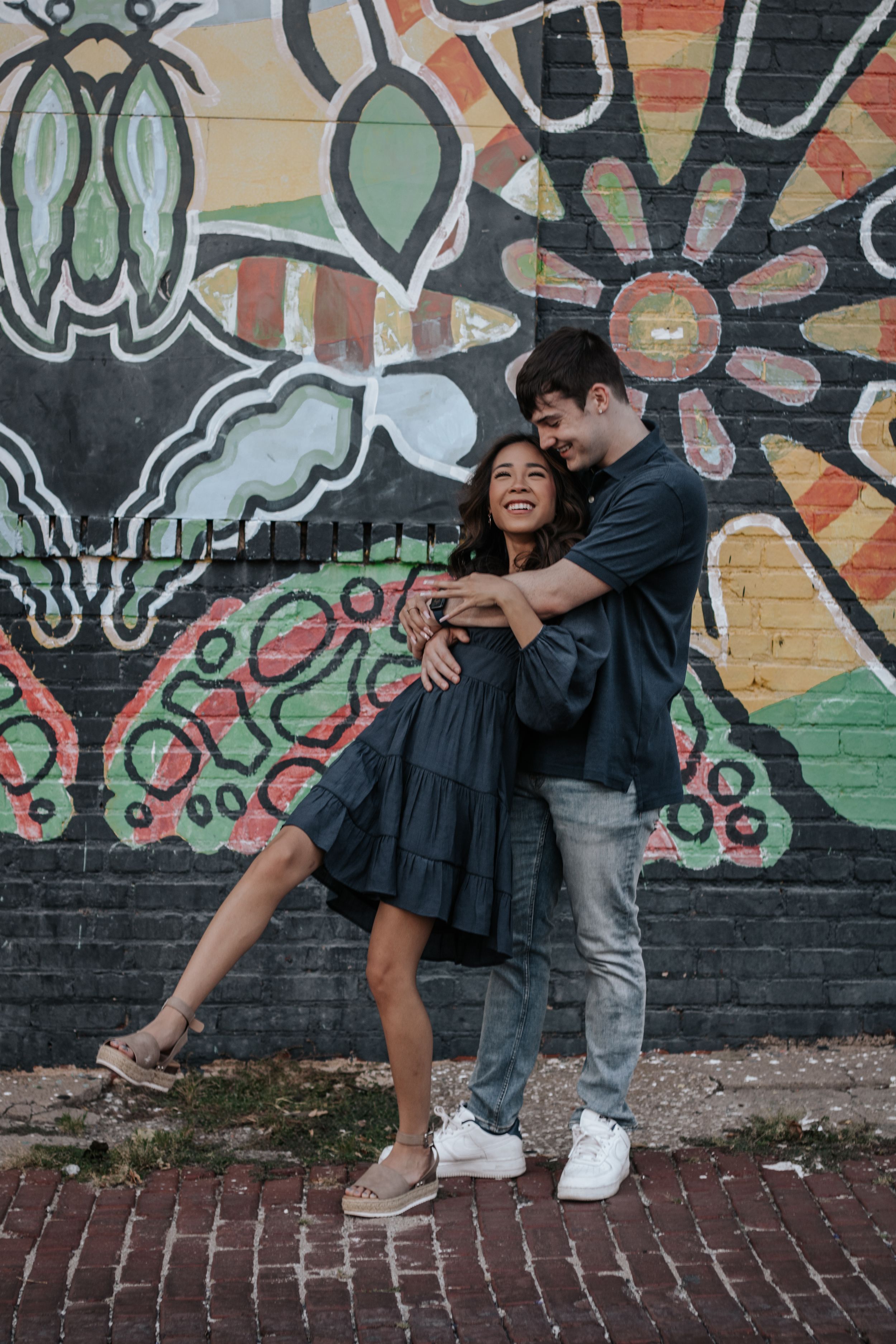 Playful couple posing and laughing against urban graffiti wall.