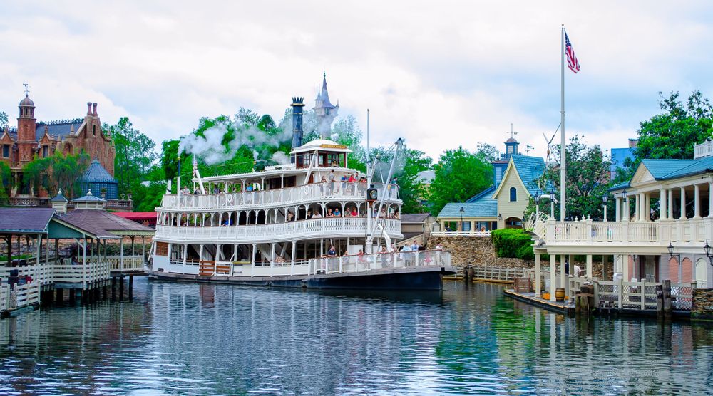 Classic riverboat cruising past waterfront buildings at a theme park.