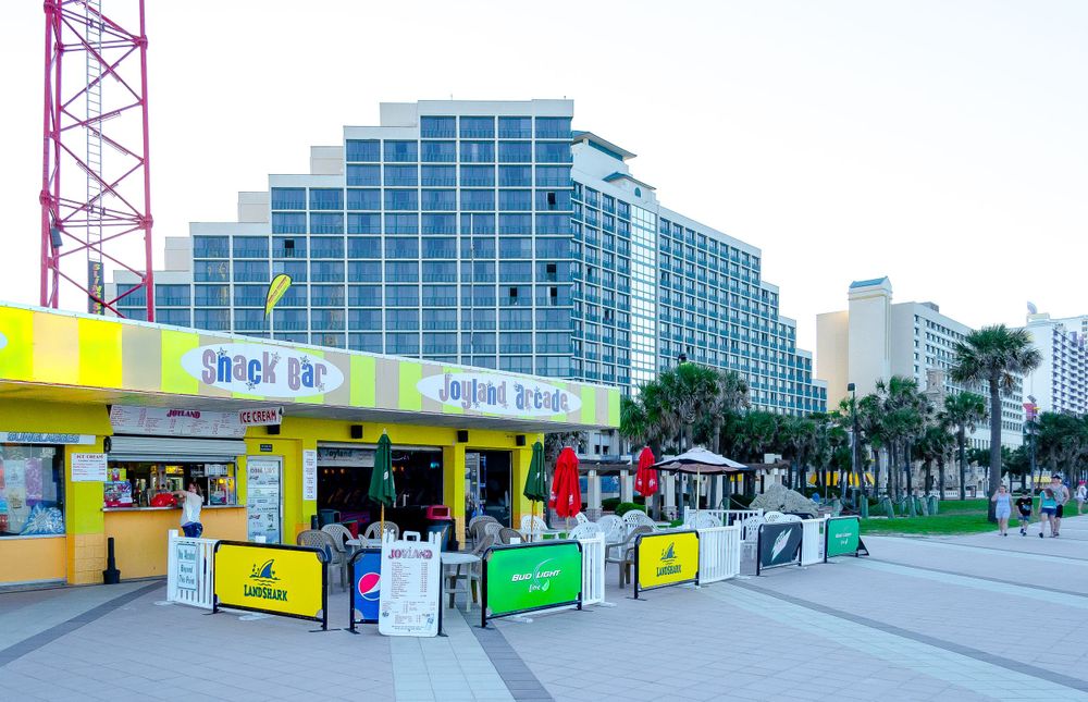 Colorful beach vendors and shops in front of modern high-rise hotels at dusk.