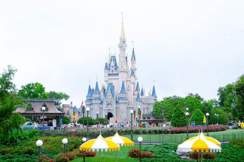 Iconic Cinderella Castle at Walt Disney World Magic Kingdom with colorful landscaping and yellow umbrellas in the foreground.