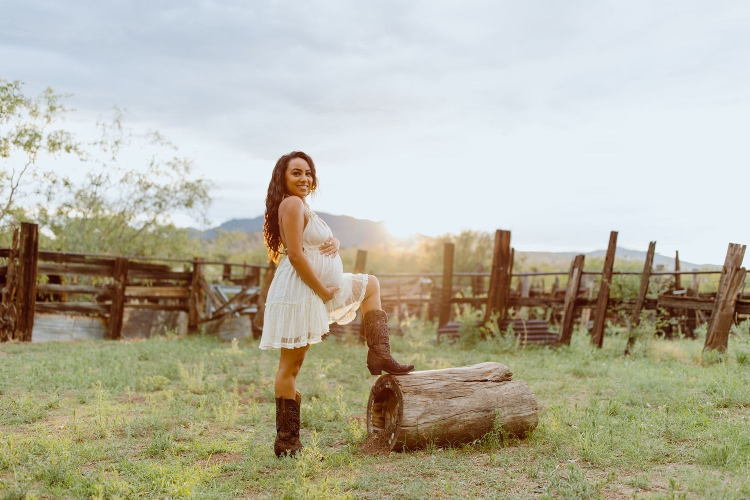 Family photoshoot in rustic field setting with wooden fence and mountain backdrop.