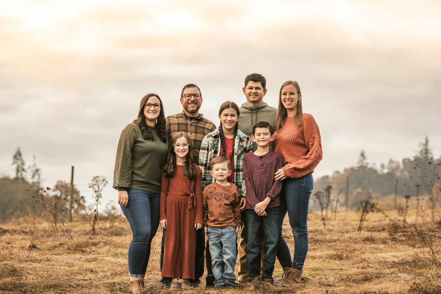 Family of 8 posed together in field all smiling and looking at camera.