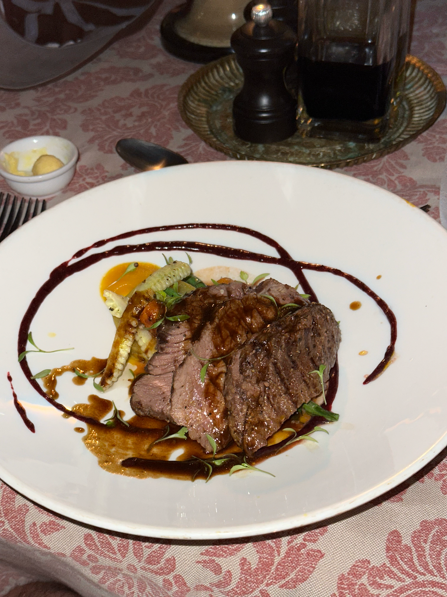 Sliced medium-rare steak served with sauce and garnish on a white plate with artistic plating.