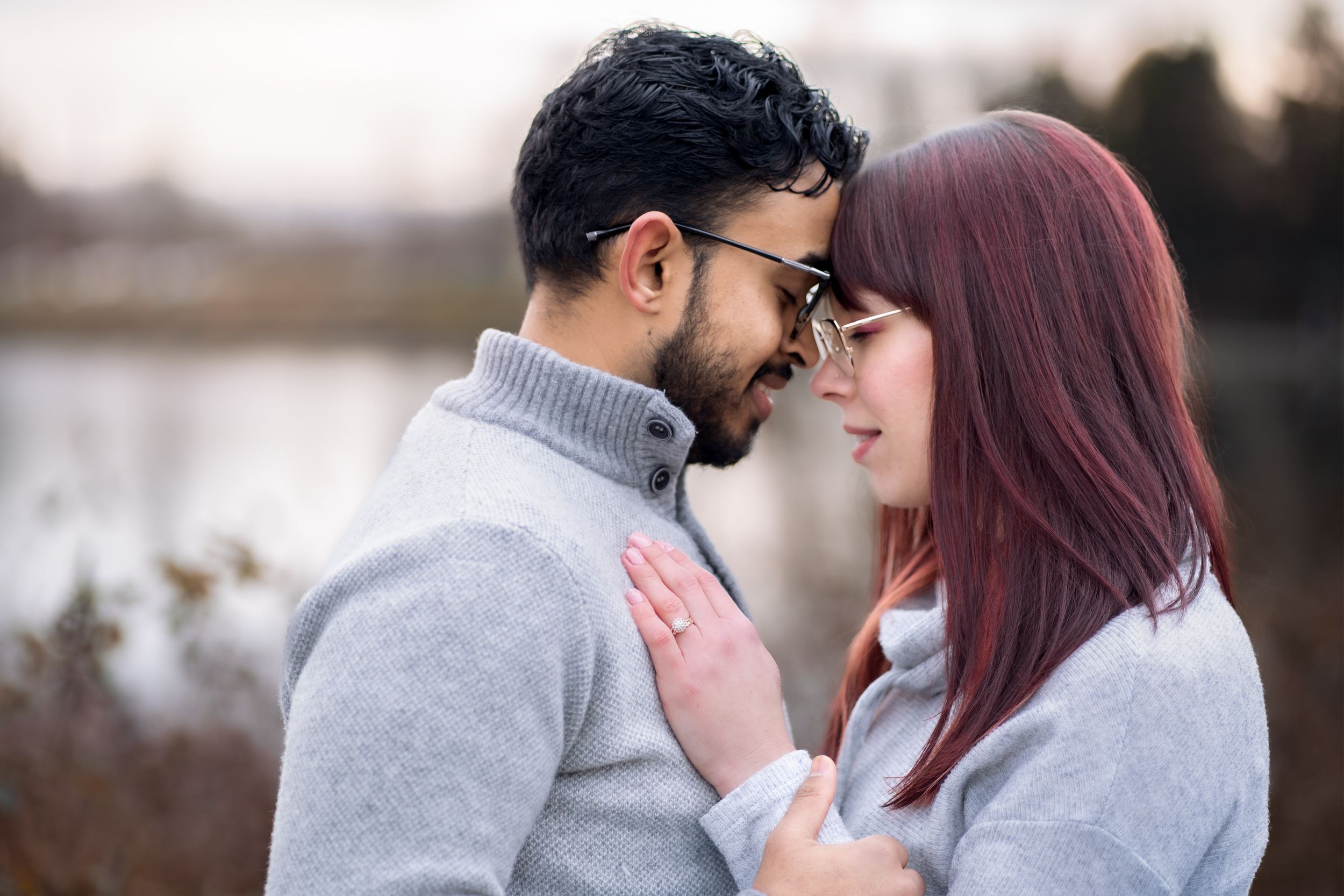 Romantic couple in matching gray sweaters sharing an intimate moment outdoors during autumn.
