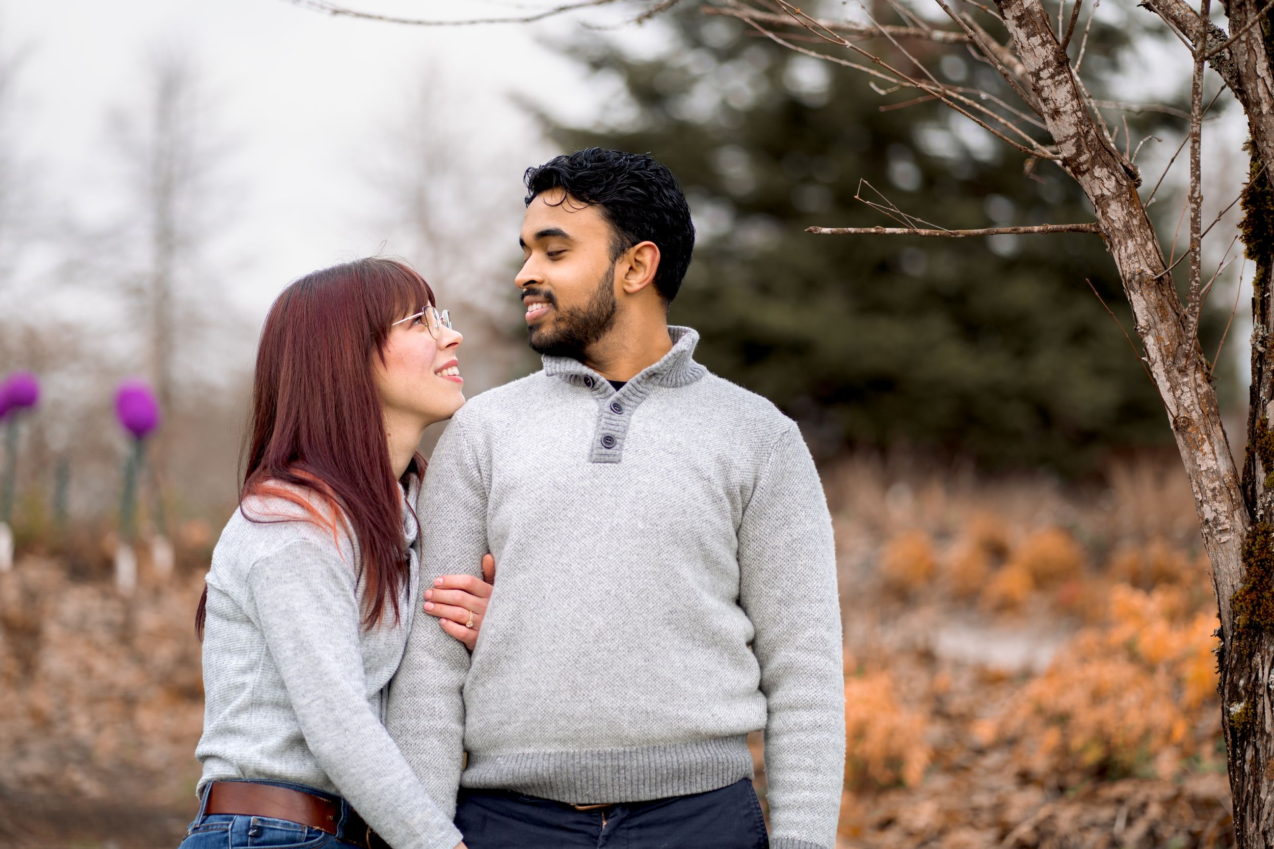 Couple laughing together in casual winter outfits against a natural fall backdrop.