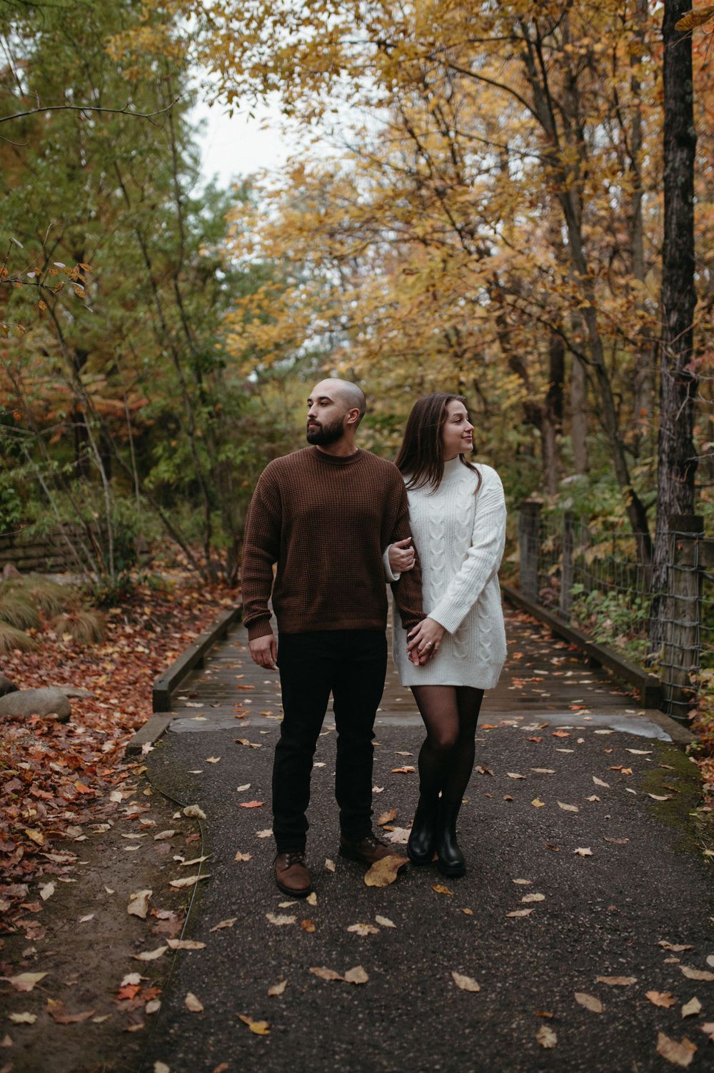 A couple walking together on a leaf-strewn path through autumn woods.